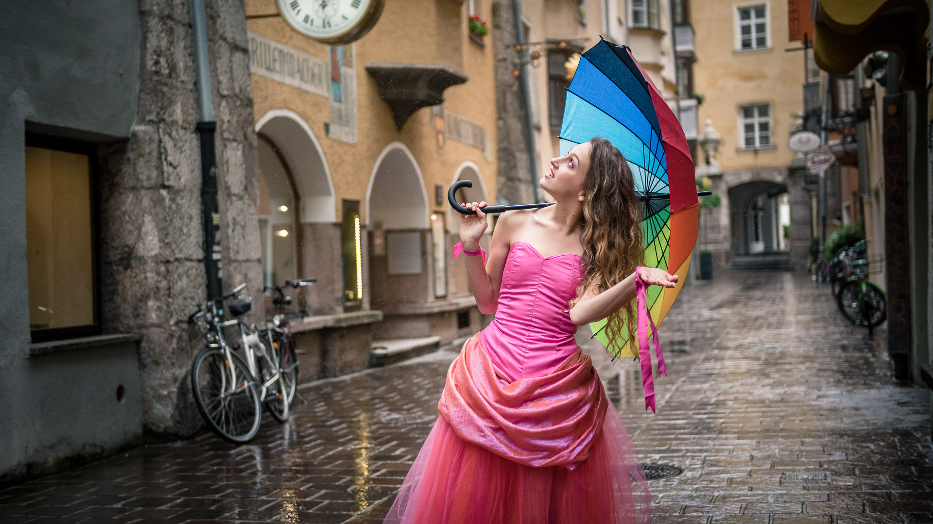 girl, pink dress, rain, umbrella, rainbow umbrella, old city, cobbled street, tulle skirt, corset