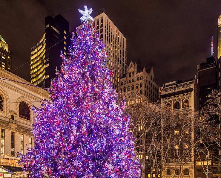The holiday tree at the Bryan Park Market in New York City glows against the skyline.